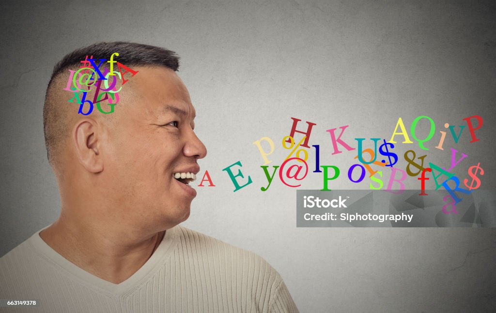 Side view portrait young handsome man talking with alphabet letters coming out of open mouth Side view portrait young handsome man talking with alphabet letters coming out of open mouth isolated grey wall background. Human face expression emotion perception. Communication concept Brain Stock Photo