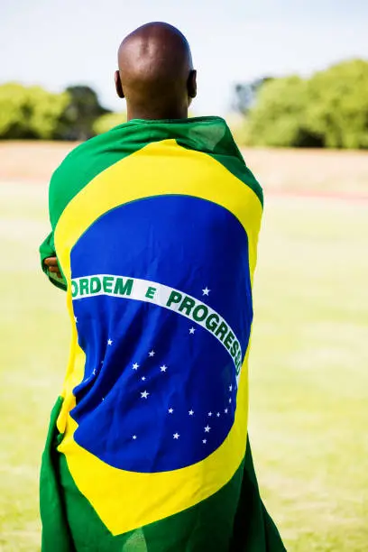 Rear view of athlete with brazilian flag wrapped around his body in stadium
