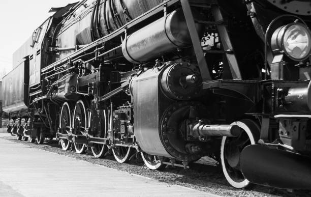 A striking black and white photograph of a series of heavy-duty cable reels on a track within an industrial setting. The image emphasizes the robust construction and mechanical design of this cable handling system.
