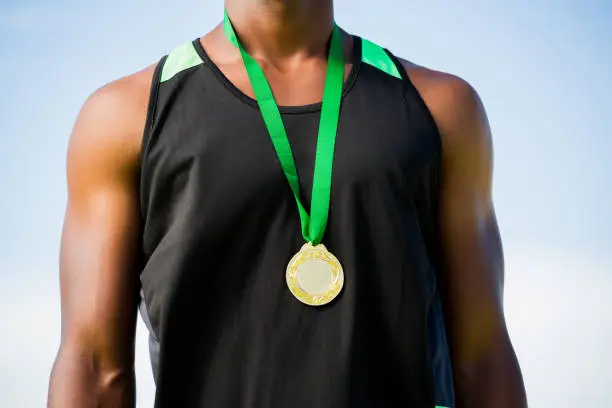 Mid section of athlete posing with gold medal around his neck on a sunny day