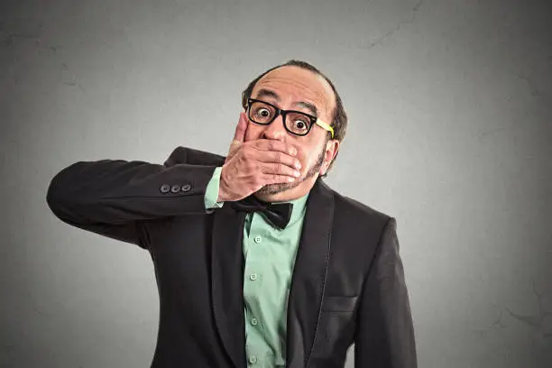 Shut up mouth, keep corporate deals secret. Portrait man worker employee covering his mouth. Speak no evil concept isolated grey background. Human emotion face expression feeling sign body language