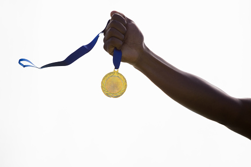 Hand of athlete holding gold medal on white background