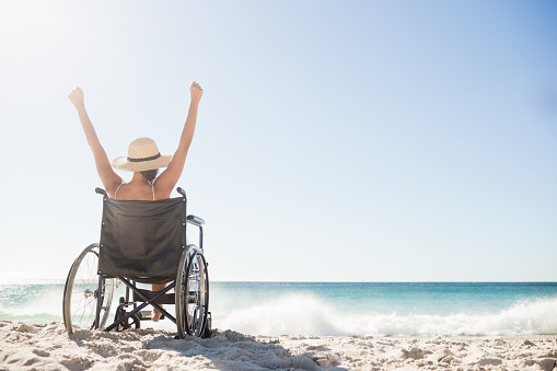 Wheelchair woman sitting  with arms up on the beach