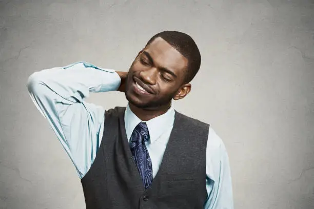 Closeup portrait, young executive man with spinal neck pain in thoracic vertebrae after long hours of work, studying, isolated grey background. Lack of ergonomic support. Face expression, feelings