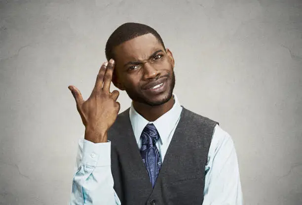 Closeup portrait rude, difficult, angry young executive businessman gesturing with fingers against temple, are you crazy? Isolated grey background. Negative human emotion, facial expression, feelings