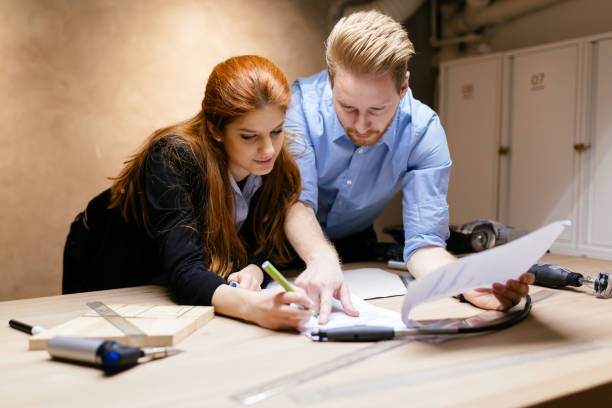 istock Creative designers working in workshop while standing at the desk full of tools and discussing ideas 663302028