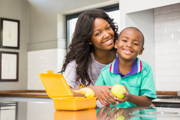 sonriente la madre preparando a hijos almuerzo escolar - healthy eating snack child domestic kitchen fotografías e imágenes de stock