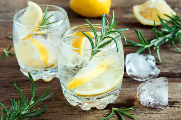 gin tonic cocktail Alcoholic drink (gin tonic cocktail) with lemon, rosemary and ice on rustic wooden table, copy space gin stock pictures, royalty-free photos & images