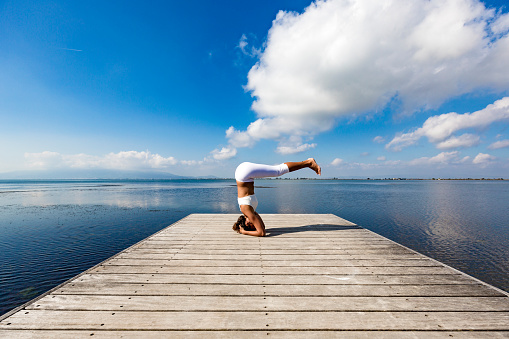 Woman doing a Yoga headstand on a pier at the sea