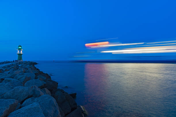 The blurred light silhouette of the ferry that enters the port of Warnemünde near the lighthouse at blue hour