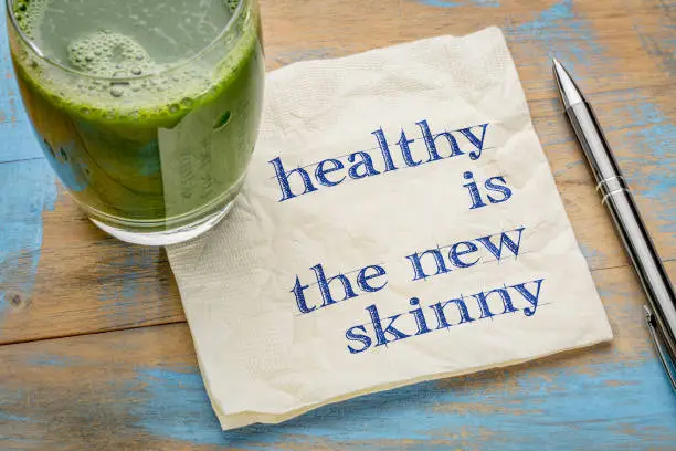 Healthy is the new skinny  - handwriting on a napkin with a glass of fresh, green, vegetable juice