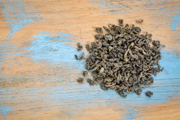 loose leaf Chinese gunpowder (pearl) green tea, a heap over grunge wood with a copy space, top view