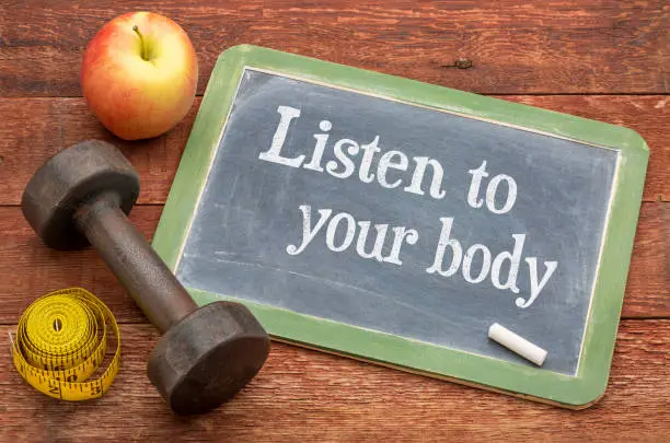 Listen to your body concept -  slate blackboard sign against weathered red painted barn wood with a dumbbell, apple and tape measure