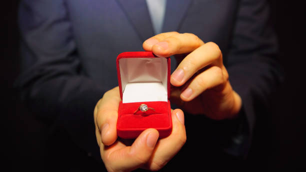 Man in a blue suit gives a ring with a diamond in a red box Man in a blue suit gives a ring with a diamond in a red box fiancé stock pictures, royalty-free photos & images