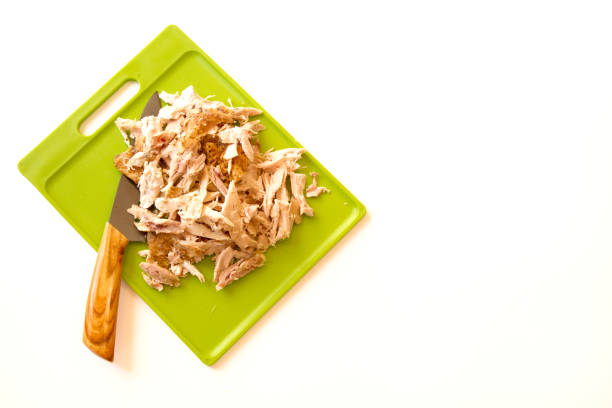 Shredded rotisserie chicken on a green cutting board and carving knife isolated on a white background with room for text or copy space