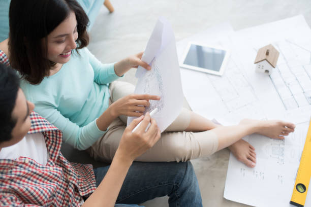 istock Cheerful asian couple looking at construction house plan 663826750