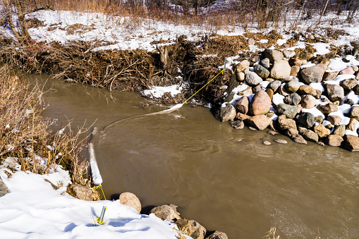 Oil absorbent boom on spring melt water run in Edmonton city creek, Alberta