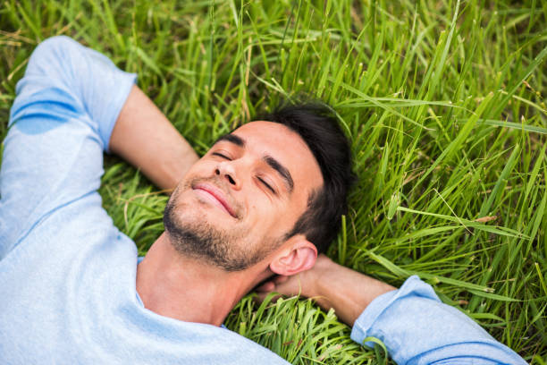 istock Beautiful young man with closed eyes, dreaming and relax on the green grass 663842036