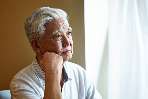 portrait of a sad asian senior man sitting by the window hand on chin.