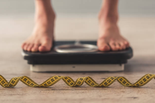 Girl and weight loss Cropped image of woman feet standing on weigh scales, on gray background. A tape measure in the foreground female rib cage stock pictures, royalty-free photos & images