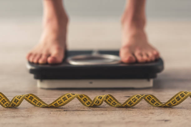 Girl and weight loss Cropped image of woman feet standing on weigh scales, on gray background. A tape measure in the foreground drug problem stock pictures, royalty-free photos & images