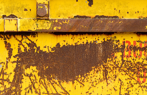 Old rusting metal skip container with yellow pealing scratched paint and orange red lettersOld rusting metal skip container with yellow pealing scratched paint and orange red letters