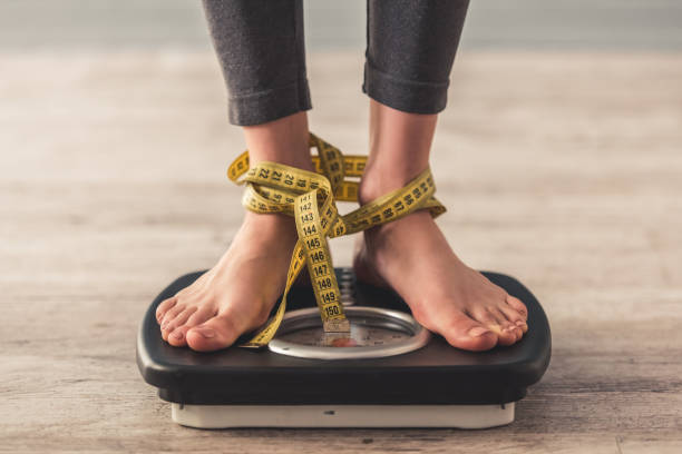 Girl and weight loss Cropped image of woman feet standing on weigh scales, on gray background. Legs winded with a tape measure photos of anorexia pictures stock pictures, royalty-free photos & images