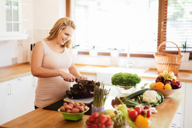 istock Pregnant woman making a meal in kitchen from fresh ingredients 663852542