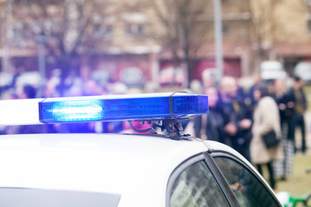 istock Police car flashing lights in focus, blurred crowd in background 663856114