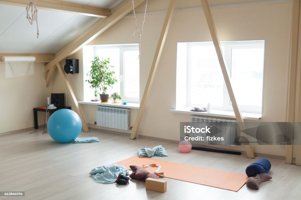Yoga class interior Empty room with fit equipment left after practice. Fitballs, sport mat, yoga props, bolsters, brick, strap, blankets on the floor in loft interior of fitness or yoga club. Healthy lifestyle concept Gym Stock Photo