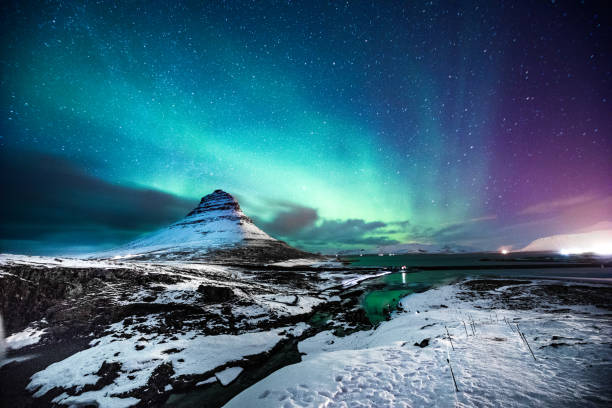 Northern lights in Mount Kirkjufell Iceland with a man passing by Solo traveler walking in front of an awesome Northern Lights in Mount Kirkjufell Iceland. iceland stock pictures, royalty-free photos & images