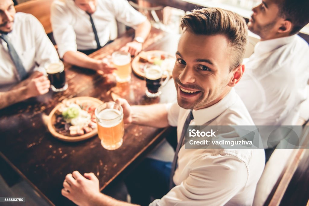 Friends in pub Handsome businessmen are drinking beer, looking at camera and smiling while resting at the pub Food Stock Photo