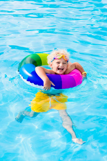 Happy little boy playing with colorful inflatable ring in outdoor swimming pool on hot summer day. Kids learn to swim. Child water toys. Children play in tropical resort. Family beach vacation.