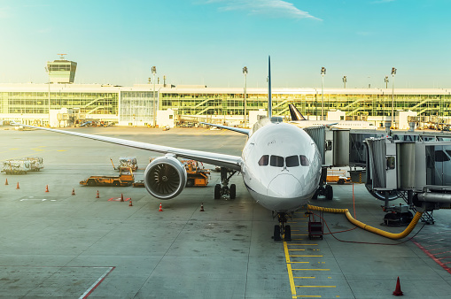 Airport, air traffic and safety concept: Airplane front view reflecting on passengers boarding corridor glass window. Jetway connecting aircraft with airport terminal gate. Jet bridge construction. Travel and Transportation theme background, copy space.