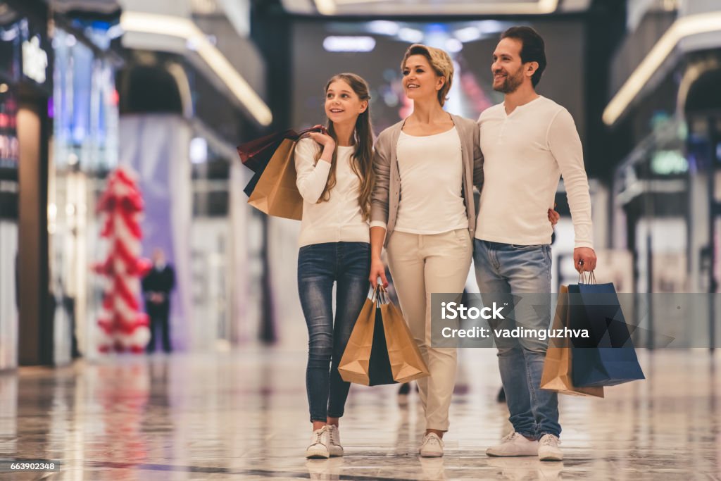 Family doing shopping Beautiful parents and their daughter are holding shopping bags and smiling while doing shopping in mall Shopping Stock Photo