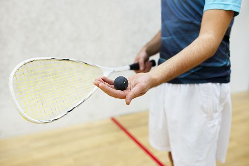 squash racket and ball in men's hand. Racquetball equipment. Photo with selective focus. Player prepares to serve a squash ball. Closeup of male hand serving ball