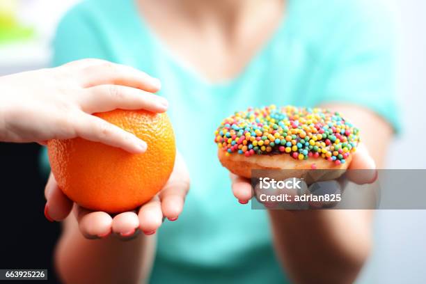 Educate Children To Choose Healthy Food Concept With Little Girl Choice To Eat Fruit Not A Donut Stock Photo - Download Image Now