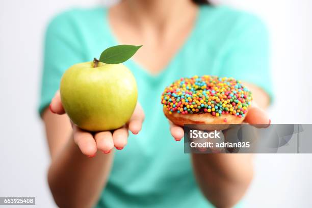 Its Hard To Choose Healthy Food Concept With Woman Hand Holding An Green Apple And A Calorie Bomb Donut Stock Photo - Download Image Now