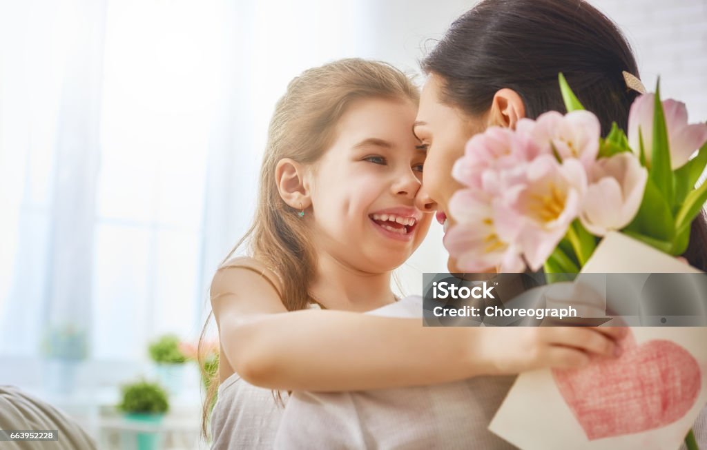 daughter congratulates mom Happy mother's day! Child daughter congratulates mom and gives her flowers tulips and postcard. Mum and girl smiling and hugging. Family holiday and togetherness. Adult Stock Photo