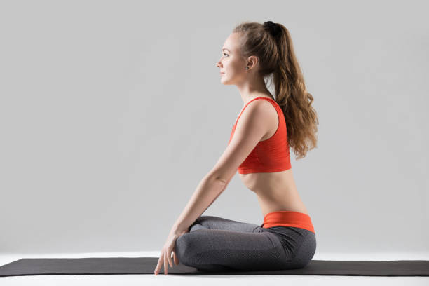 Young attractive woman in Upward Abdominal Lock pose, grey studi Young attractive woman practicing yoga, sitting in Sukhasana exercise, making Upward Abdominal Lock, Uddiyana Bandha, working out, wearing sportswear, red sports bra, pants, full length, grey studio sukhasana stock pictures, royalty-free photos & images