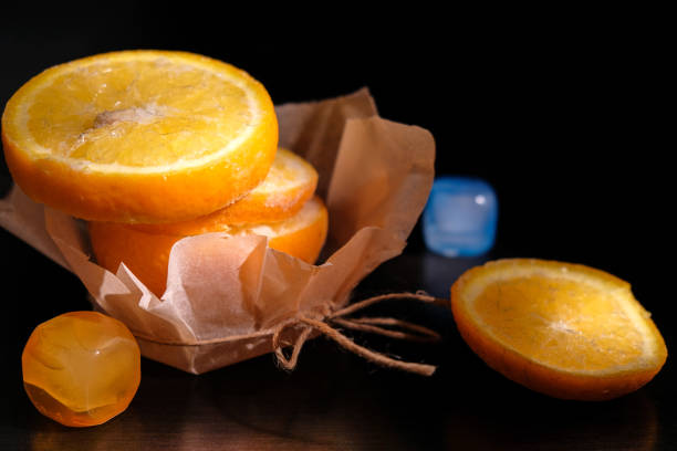 istock frozen fresh orange on black table sliced and stacked on one another stand on paper wrapper except top which lay near on surface and add two plastic ice cube lighting by spot/main object change 664000184
