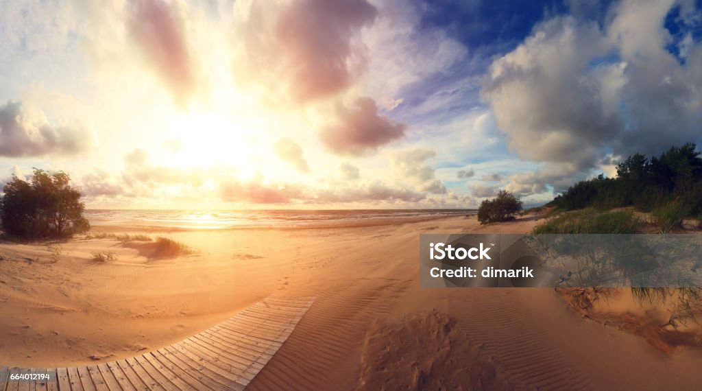 South coast at the sunset Sunset at south beach. South coast at the sunset. Bright evening sun shines at golden sand. Wooden path on beach. Beautiful resort background. Beach Stock Photo