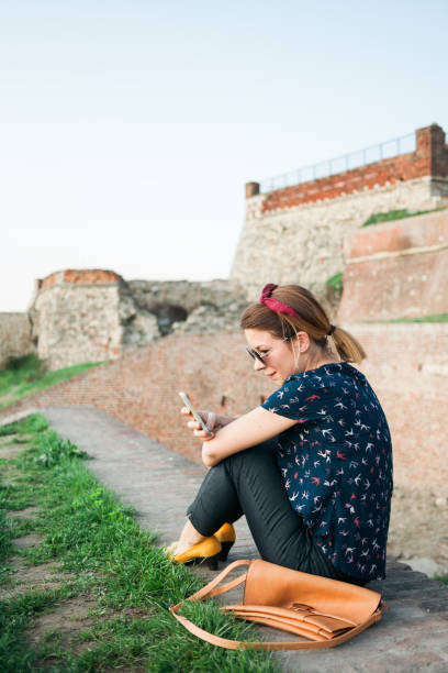 istock Young woman sitting in the park using smartphone 664015710