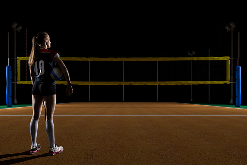 Female volleyball player holding the ball on volleyball field at night