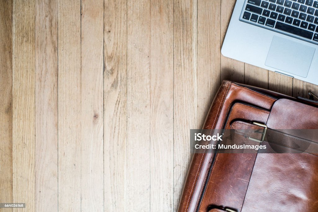 Laptop and Briefcase on a desk from above. A shot of a laptop and leather briefcase shot from above in a studio.Focus on briefcase. Briefcase Stock Photo