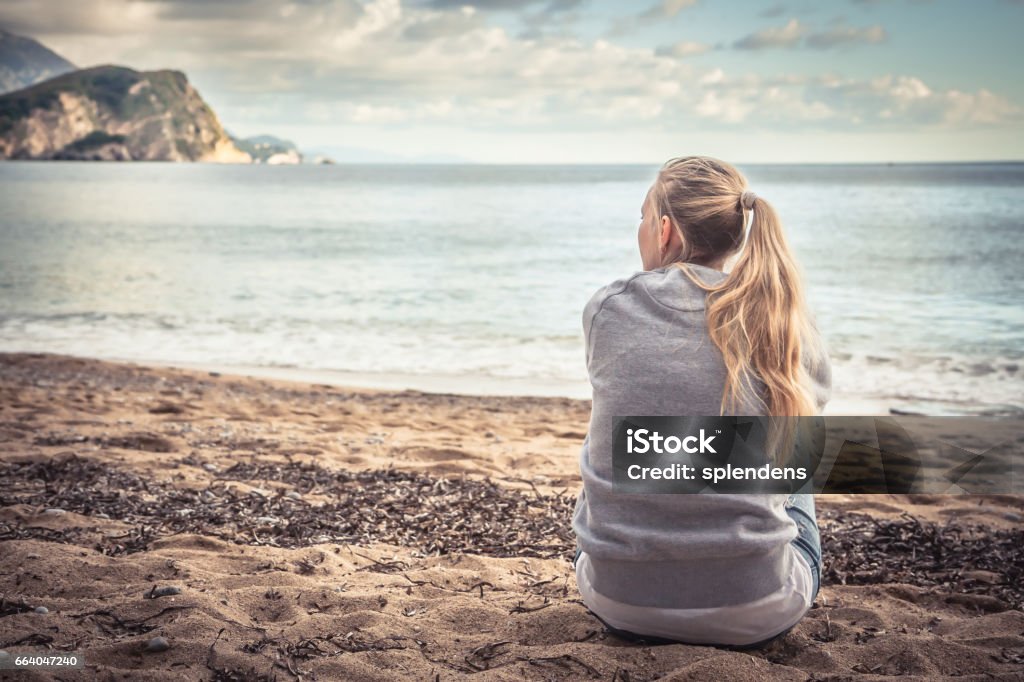 Songeuse solitaire jeune femme assise sur la plage de serrant ses genoux et à la recherche dans le lointain avec espoir - Photo de Femmes libre de droits