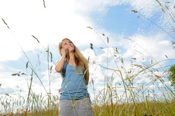happy young blond woman with smartphone on  flower meadow