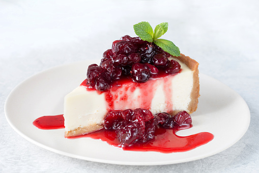 Cheesecake with sour cherry sauce and mint leaf on white plate. Isolated