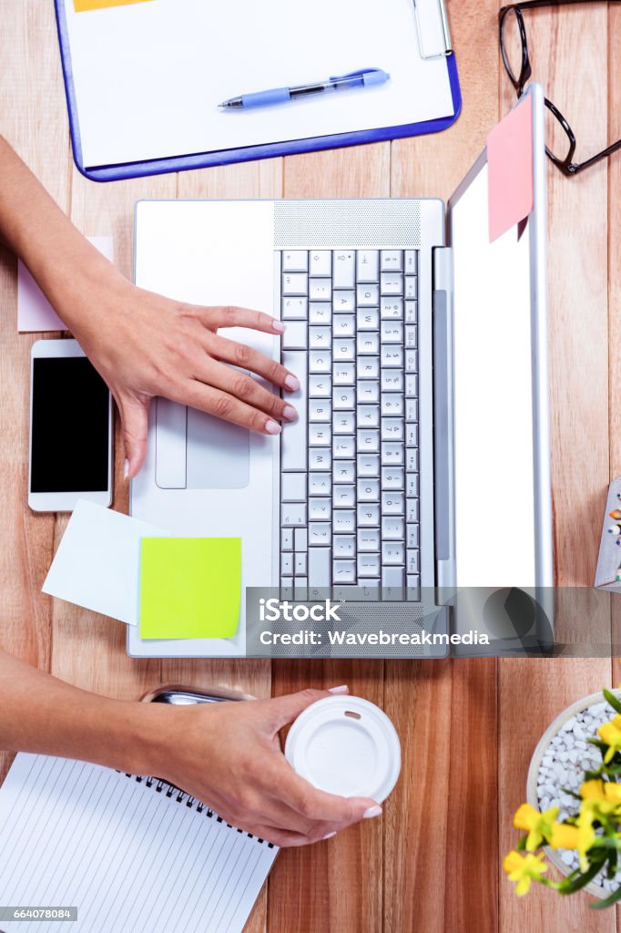 Overhead of feminine hands using laptop and holding coffee mug Overhead of feminine hands using laptop and holding coffee mug with stuff on desk Coffee - Drink Stock Photo