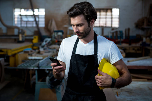 istock Carpenter texting someone and holding his helmet 664087814